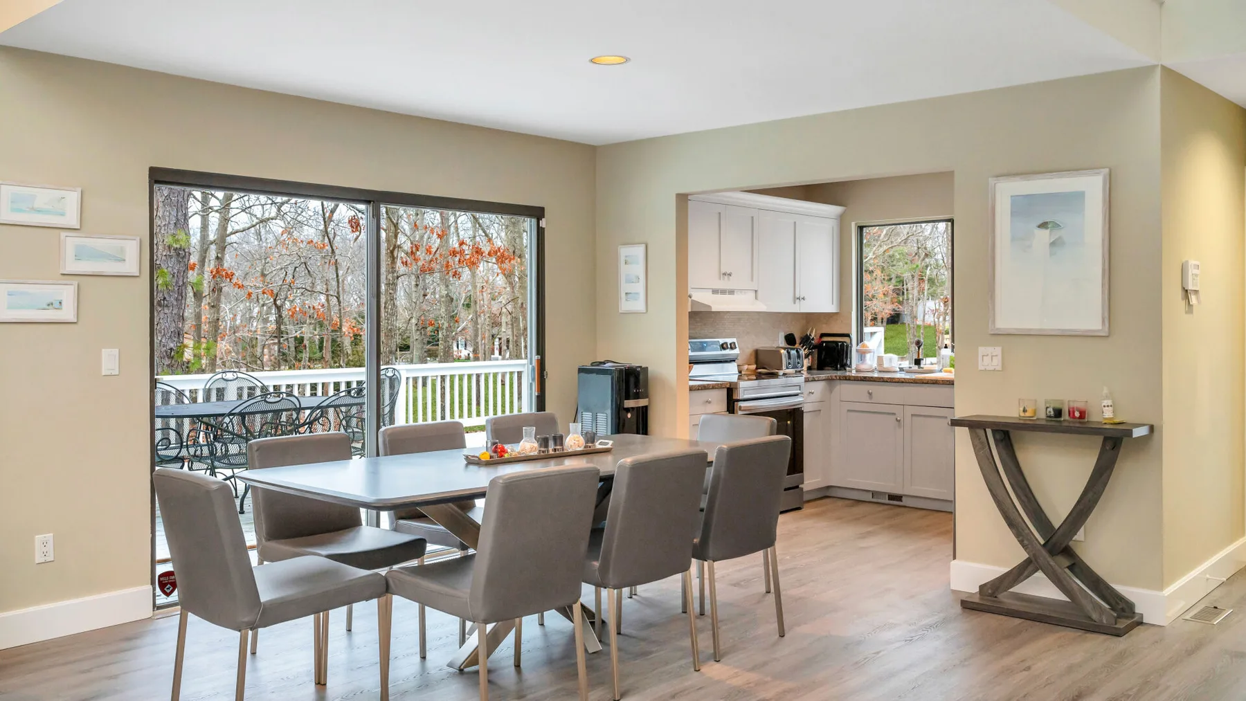 Comedor con mesa y asientos junto a una cocina y ventanas grandes.