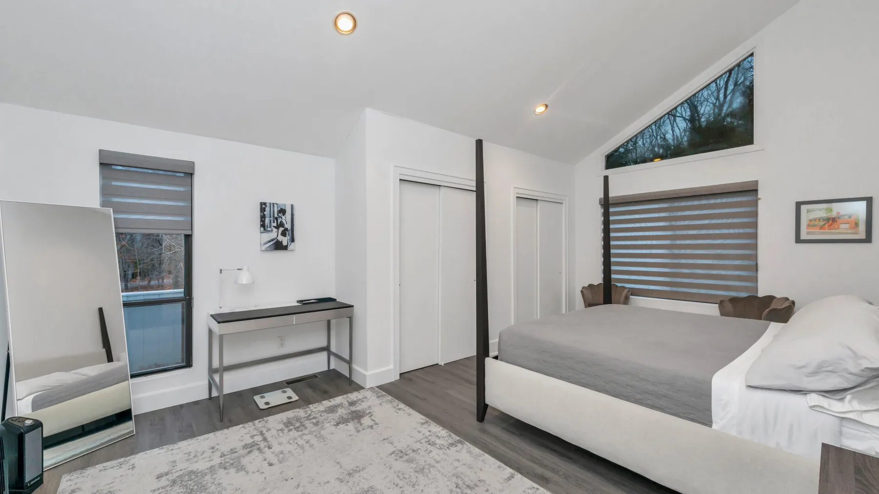 Un dormitorio luminoso con una cama, ropa de cama gris y una ventana grande.