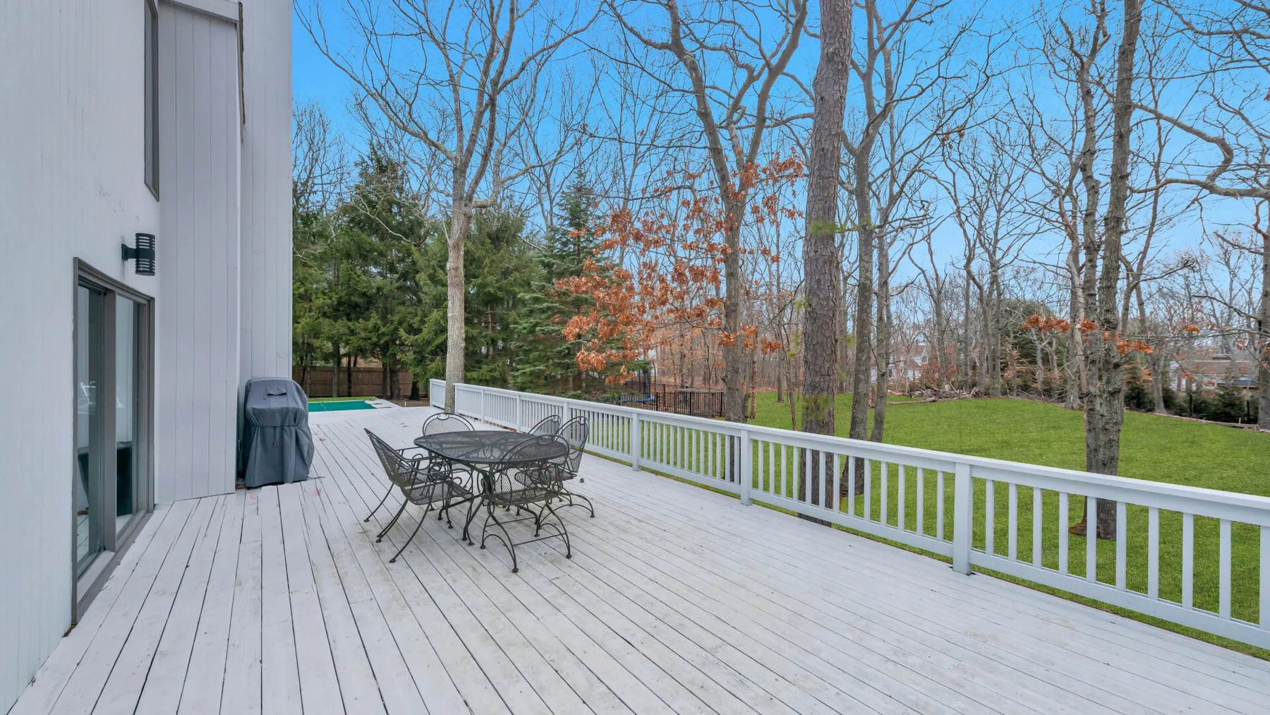 Una terraza exterior con mesa y sillas de comedor da a un patio con césped.