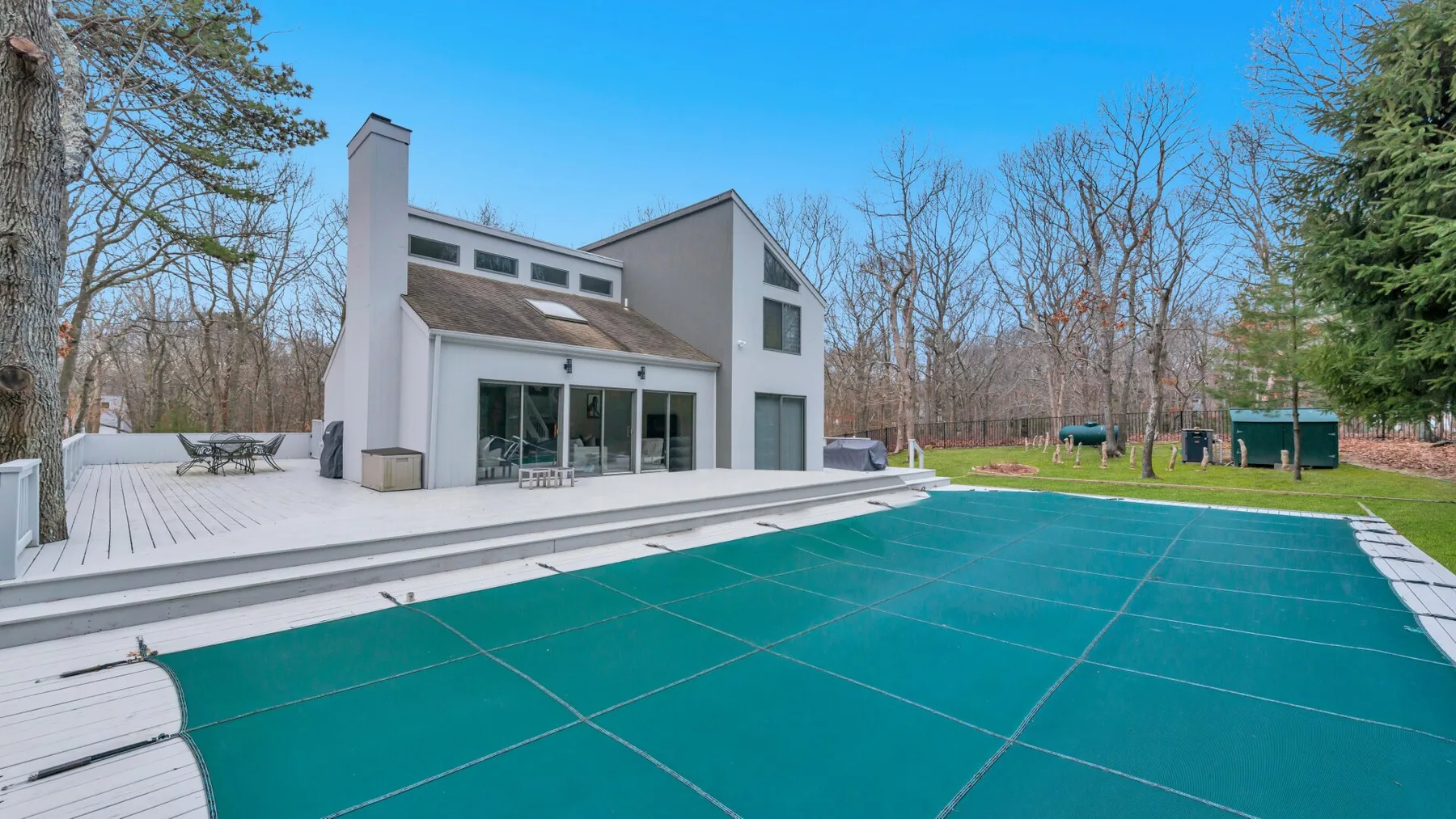 Una casa moderna está junto a una piscina cubierta y un patio ajardinado.