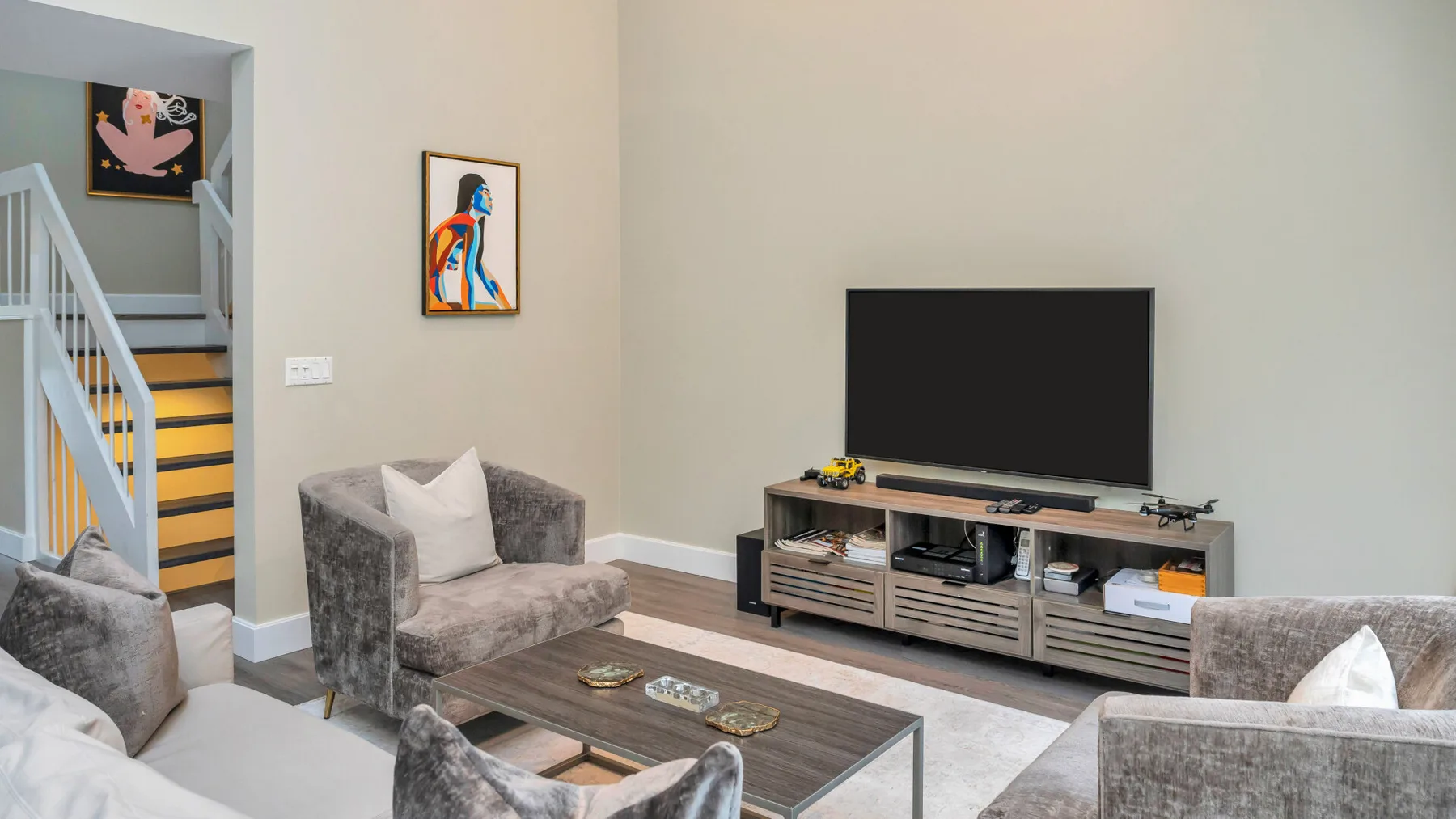 Una sala de estar con asientos grises, un televisor y un mueble bajo.