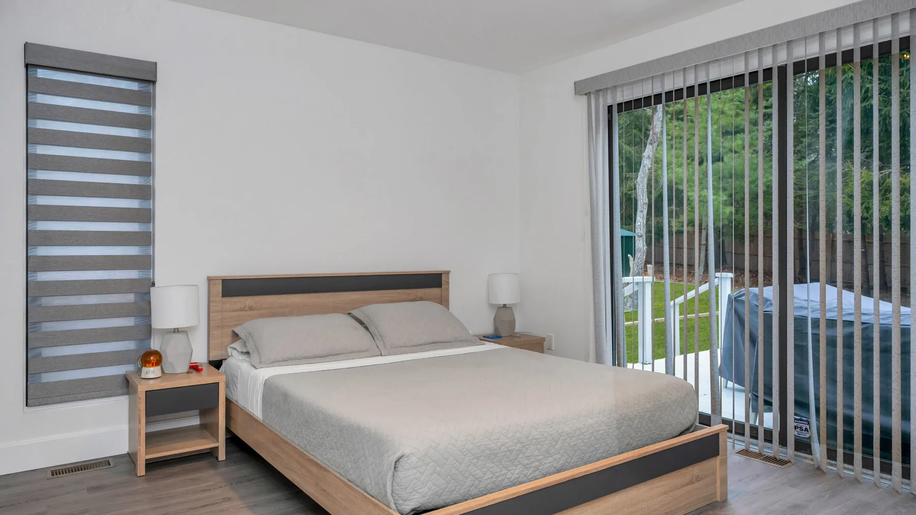 Un dormitorio con una cama bien tendida y persianas verticales frente a una ventana grande.
