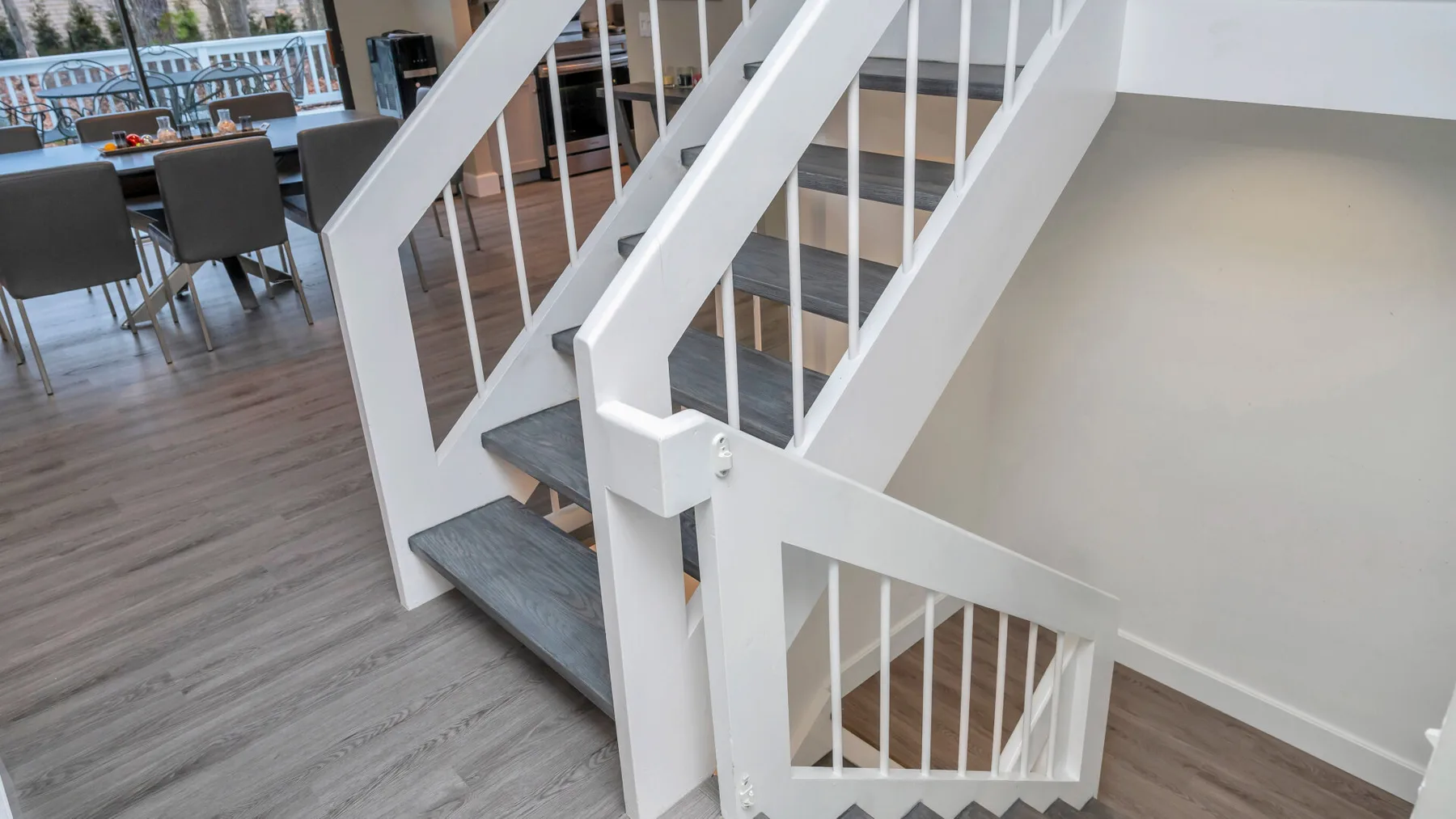 Una escalera blanca con peldaños grises junto a un comedor.
