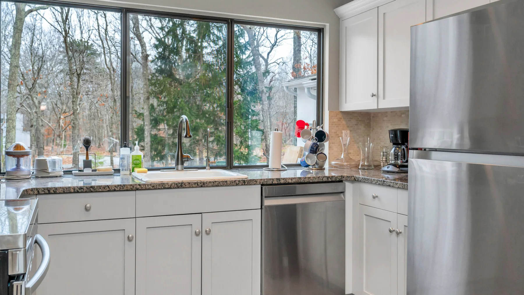 Una cocina luminosa con gabinetes blancos y una ventana grande con vista a los árboles.