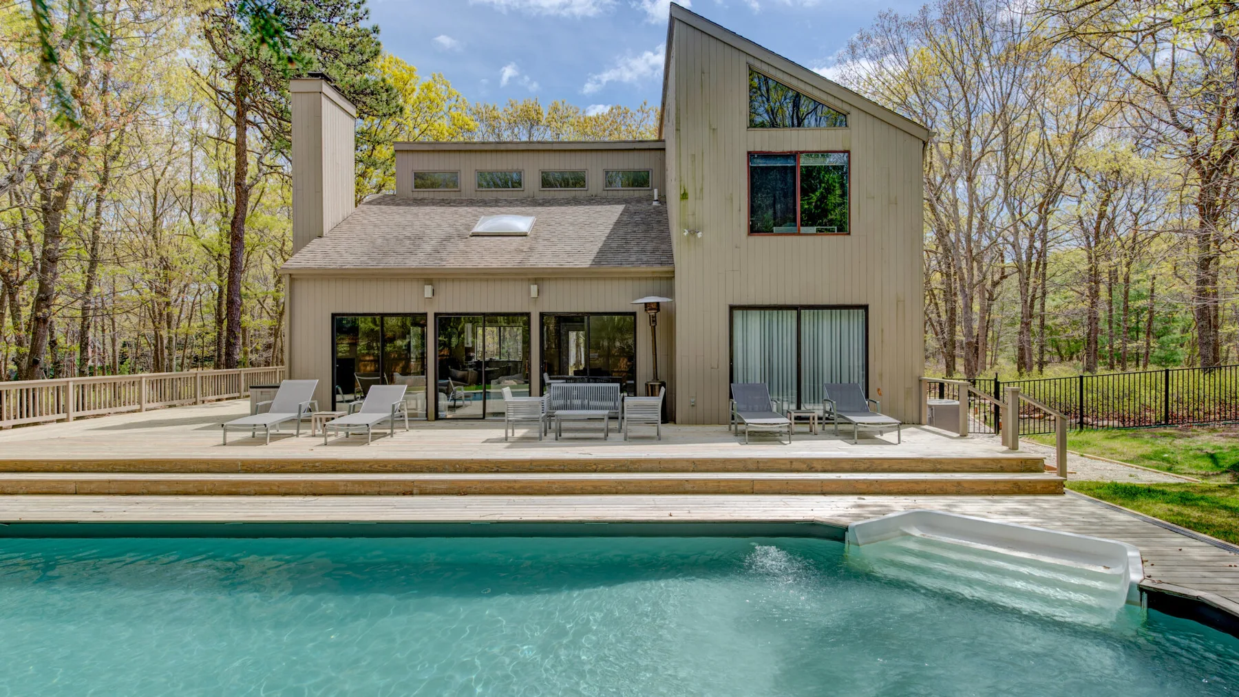 Una casa moderna está junto a una piscina, rodeada de árboles.