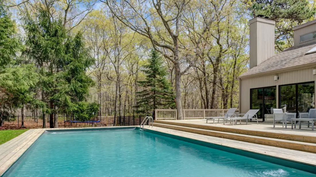 Una piscina al aire libre junto a una casa, con árboles alrededor del patio.
