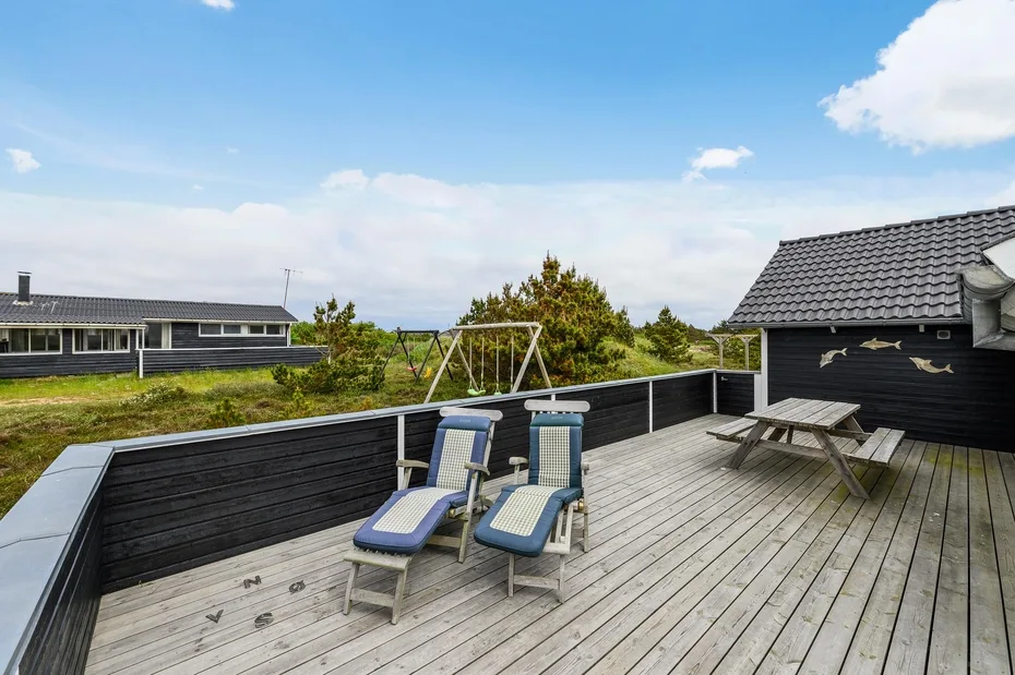 Outdoor deck with two reclining seats and a picnic table beside a dark building.