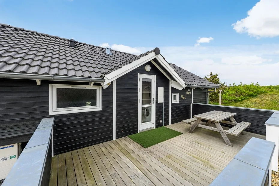 A wooden deck outside a dark-sided house, with a picnic table beside the door.