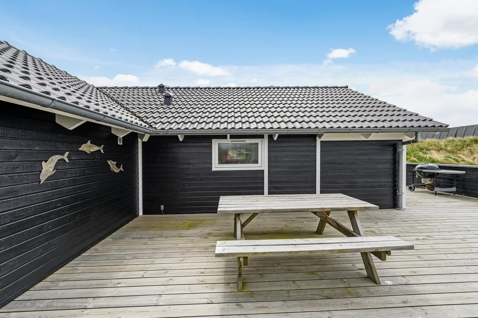 A wooden deck with a picnic table sits beside a dark-sided building.