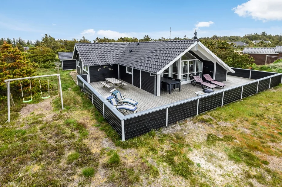 A dark-sided house with a broad wooden deck and outdoor seating.