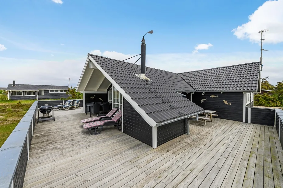 A rooftop deck with outdoor seating beside a dark, pitched-roof structure.