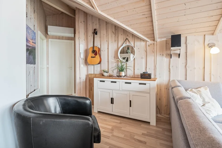 A bright wood-paneled living room with a cabinet, guitar, and seating.