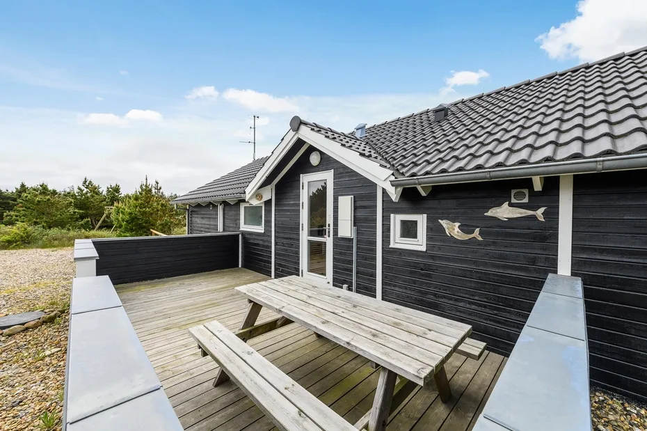 A wooden deck with a picnic table sits beside a dark-sided house.