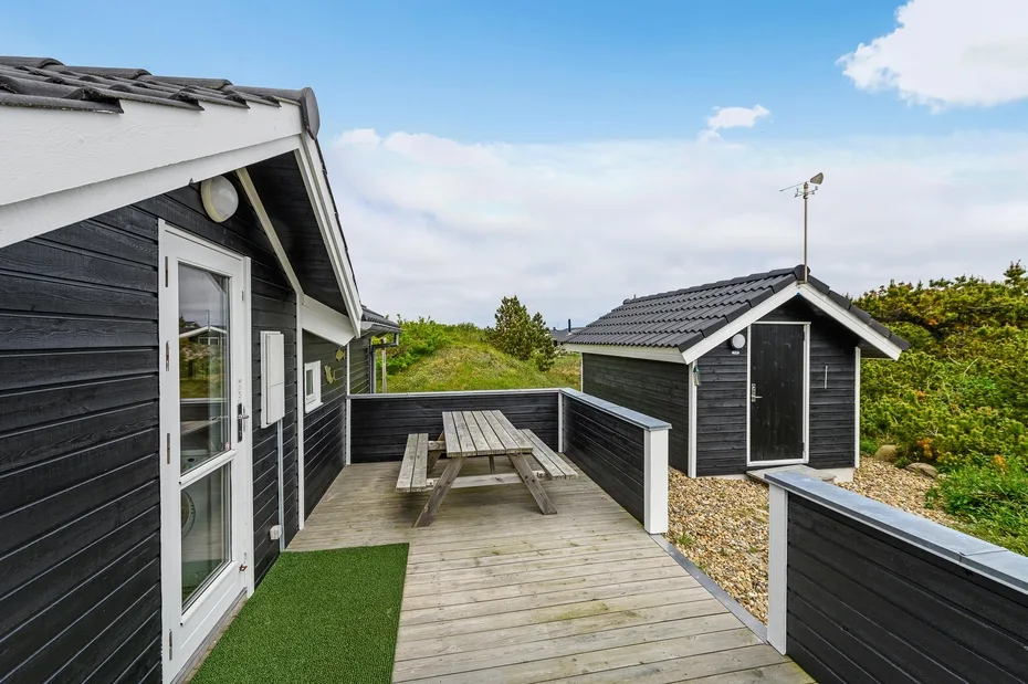 A wooden outdoor deck with a picnic table beside dark-sided buildings.