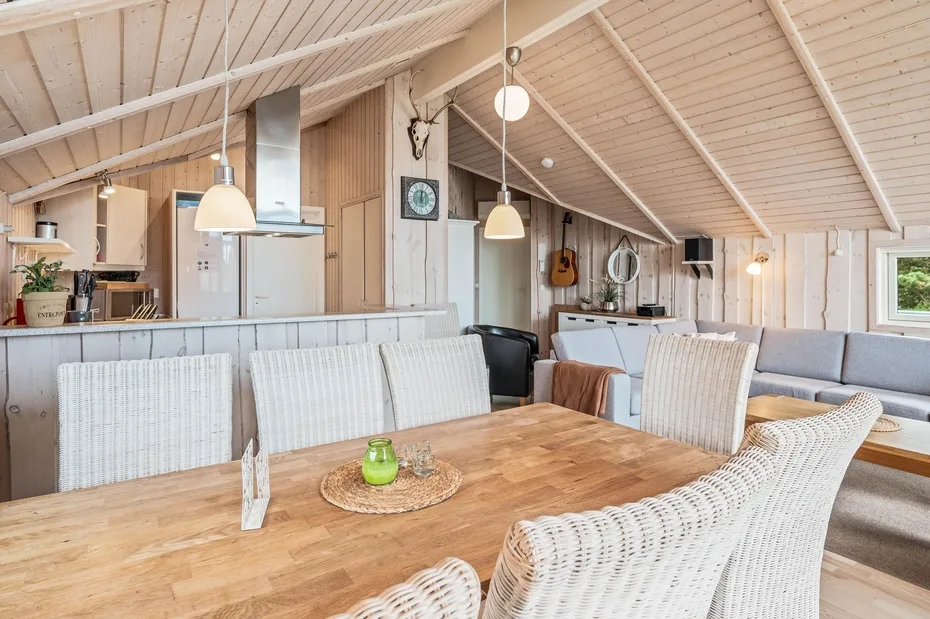 A dining area with a wooden table and white woven seating beneath a sloped ceiling.