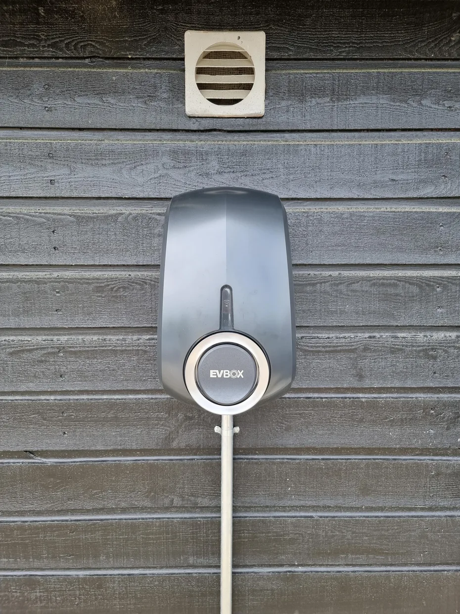 An electric vehicle charging unit is mounted on a gray wooden exterior wall.