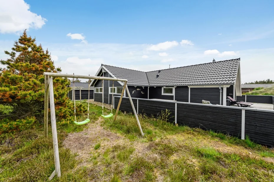 An outdoor yard with a swing set beside a dark-sided house.