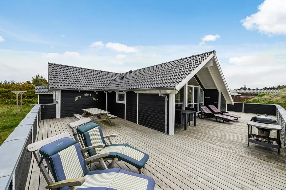 A spacious rooftop terrace beside a dark wood house, with lounge seating and a clear sky.