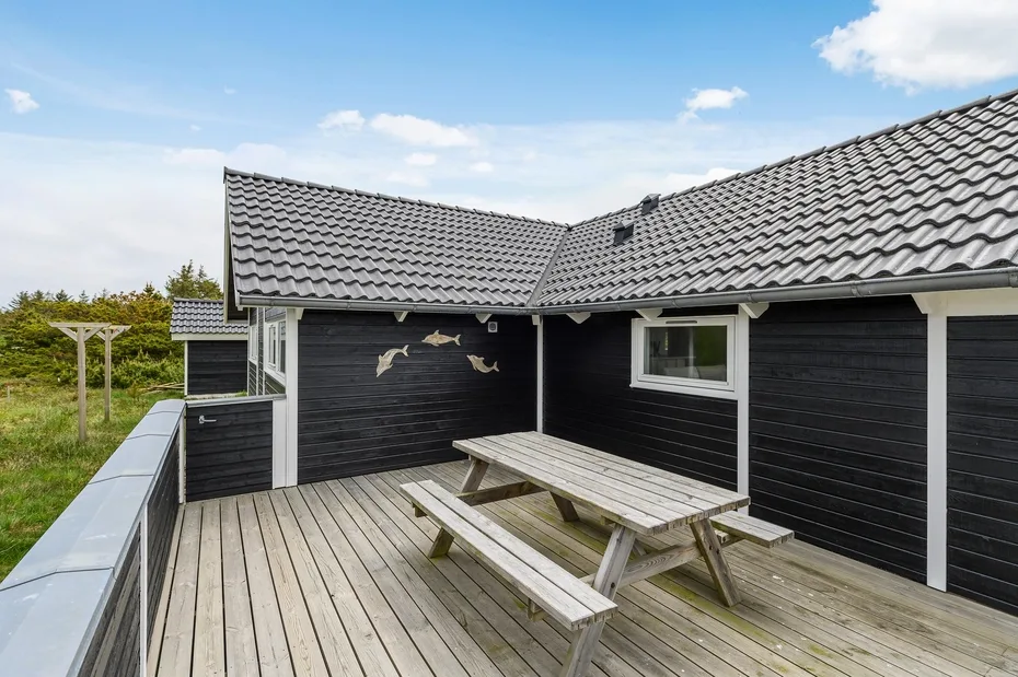 A wooden deck beside a dark-sided building has a picnic table and small window.
