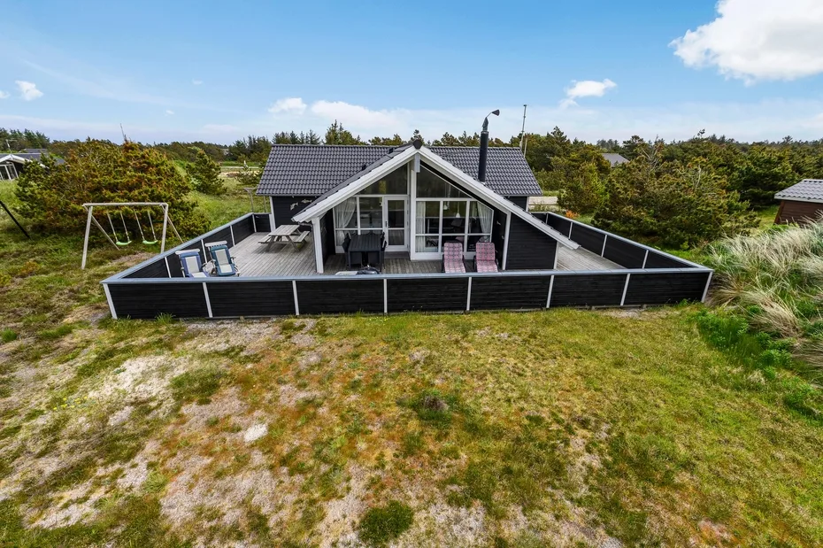 A modern house with a fenced patio sits amid open grassy grounds.