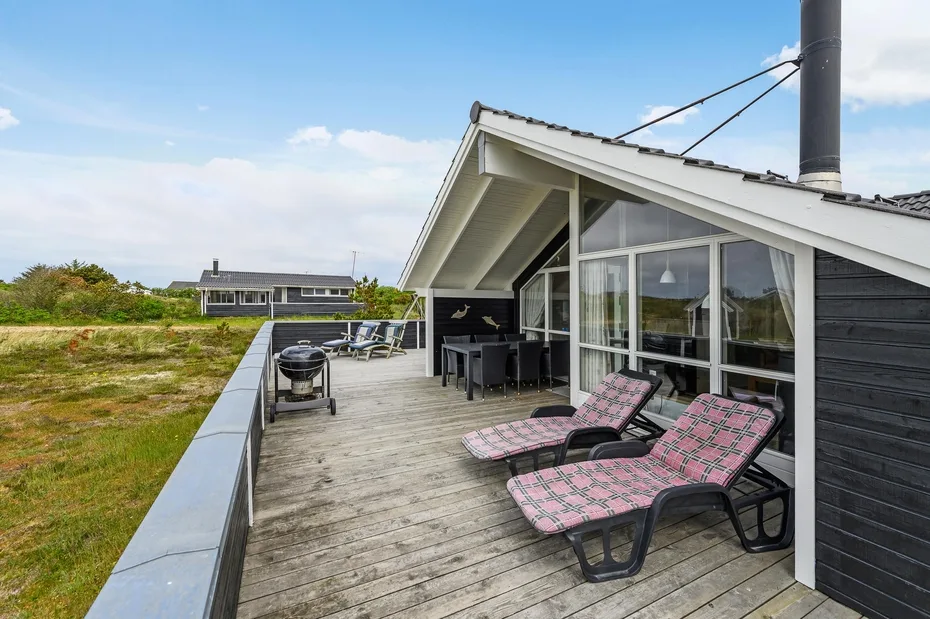 A wooden deck beside a modern house has outdoor seating and a grill.