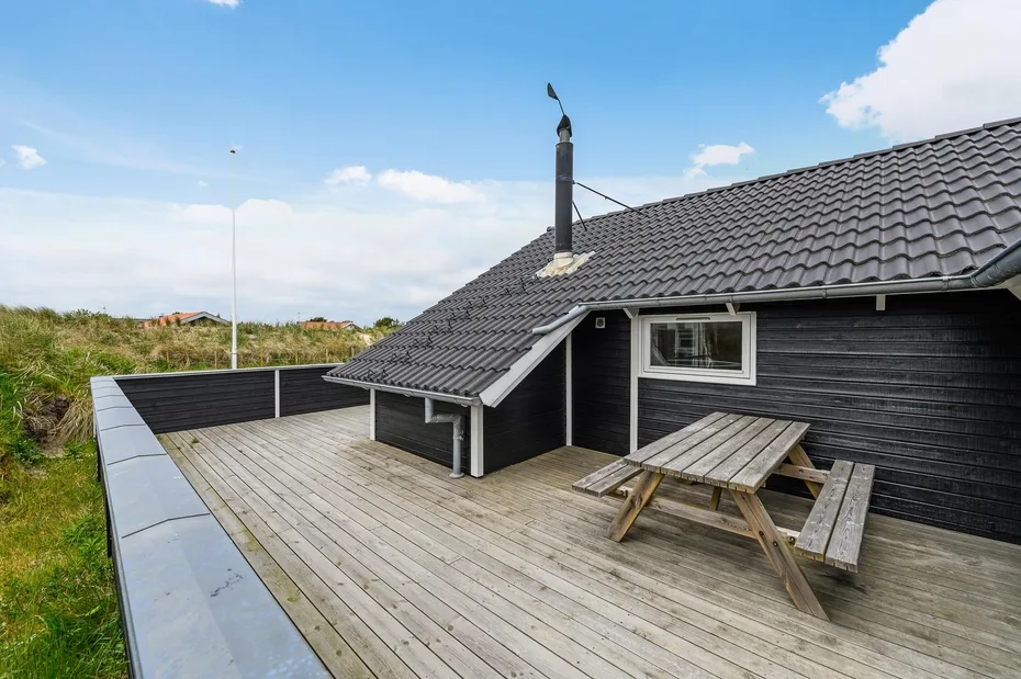 A wooden deck beside a dark exterior wall features a picnic table and roof.
