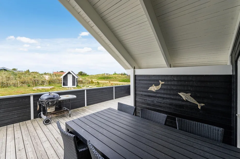 A covered outdoor deck with a dark dining table and barbecue overlooking open greenery.
