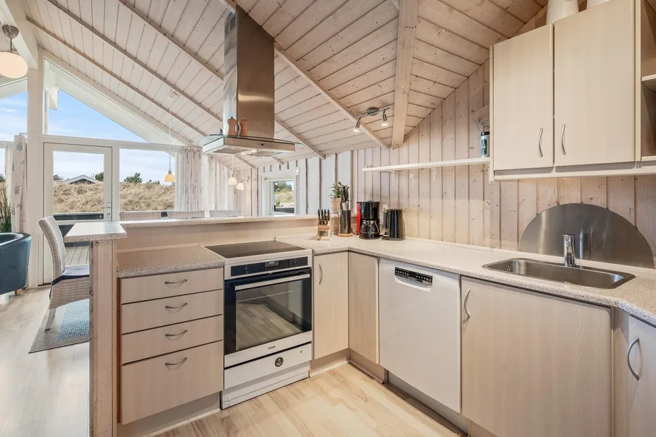 A bright kitchen with light wood cabinets, a stove, and a sink.