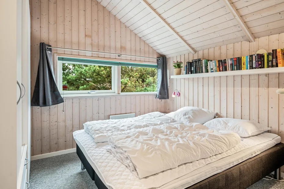 A bedroom with a bed beneath a window and a shelf of books.