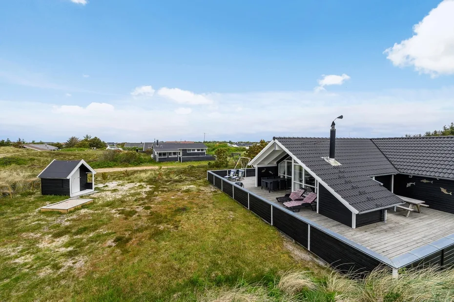 A modern house with a broad deck sits in an open grassy landscape.