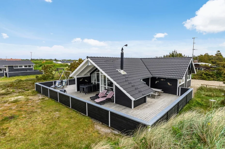 A dark-roofed house with a spacious wooden deck and outdoor seating.