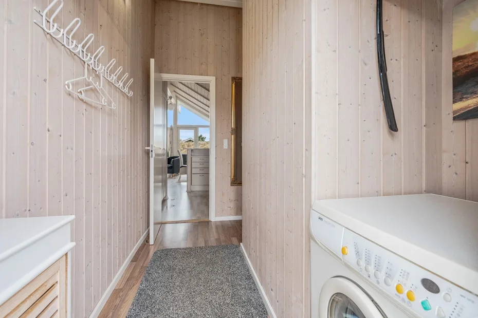 A narrow utility room with a washing machine and wall-mounted coat hooks.