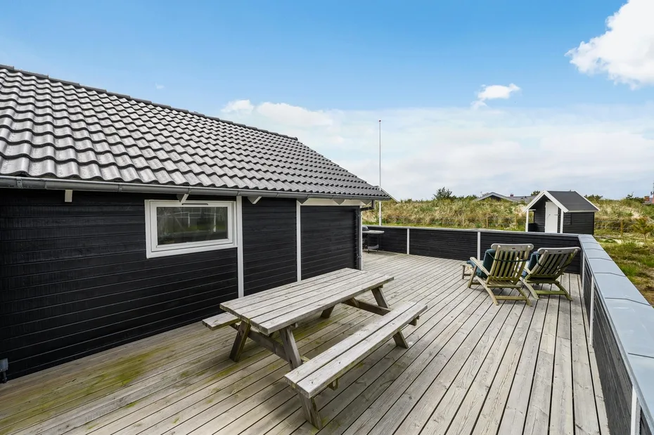 A wooden deck beside a dark-sided building has picnic seating and a view of the sky.