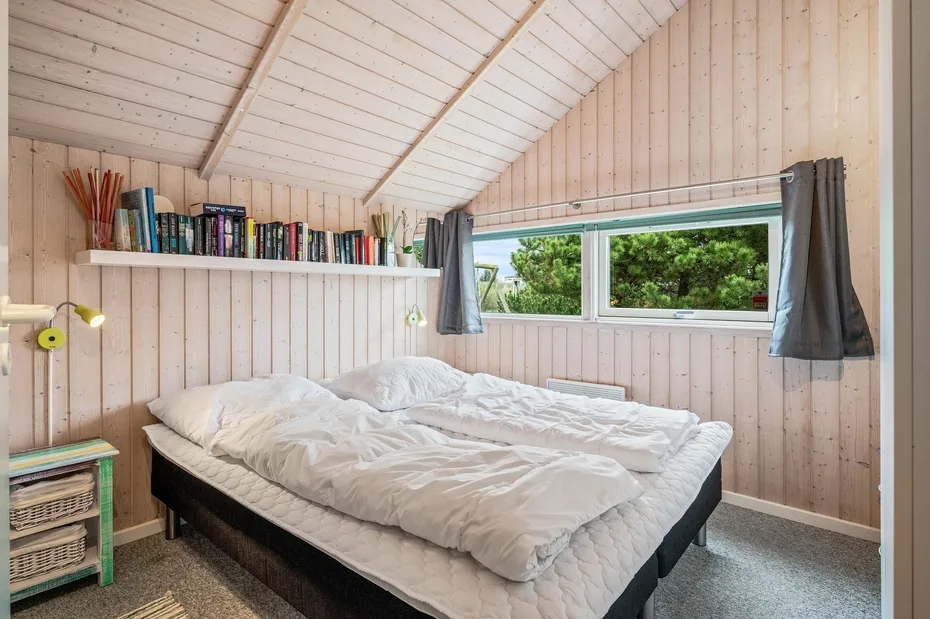 A bedroom with a bed beneath a wide window overlooking greenery.