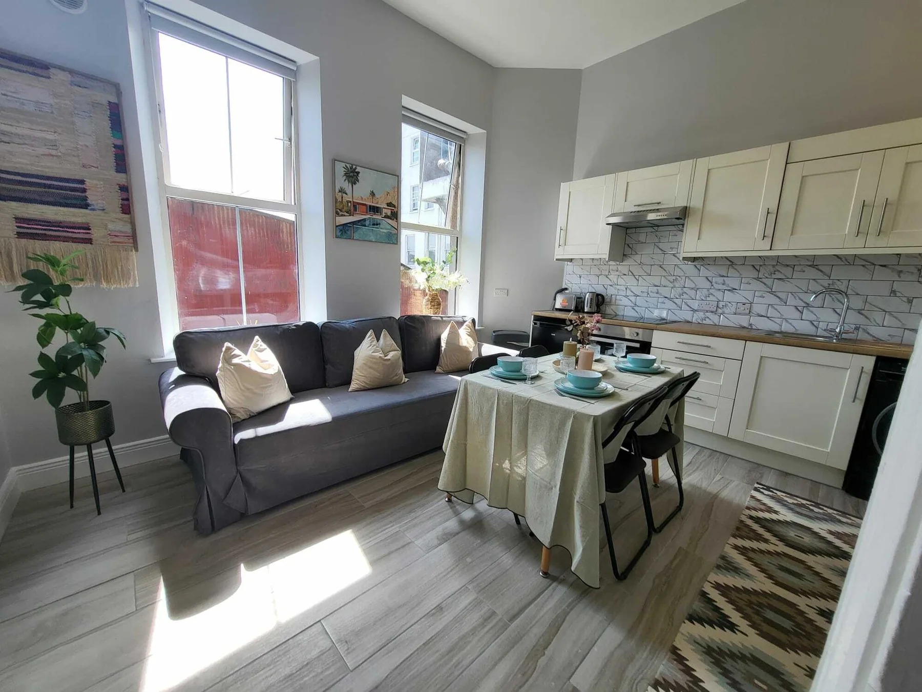 A living area with a dark sofa beside a dining table and kitchen.