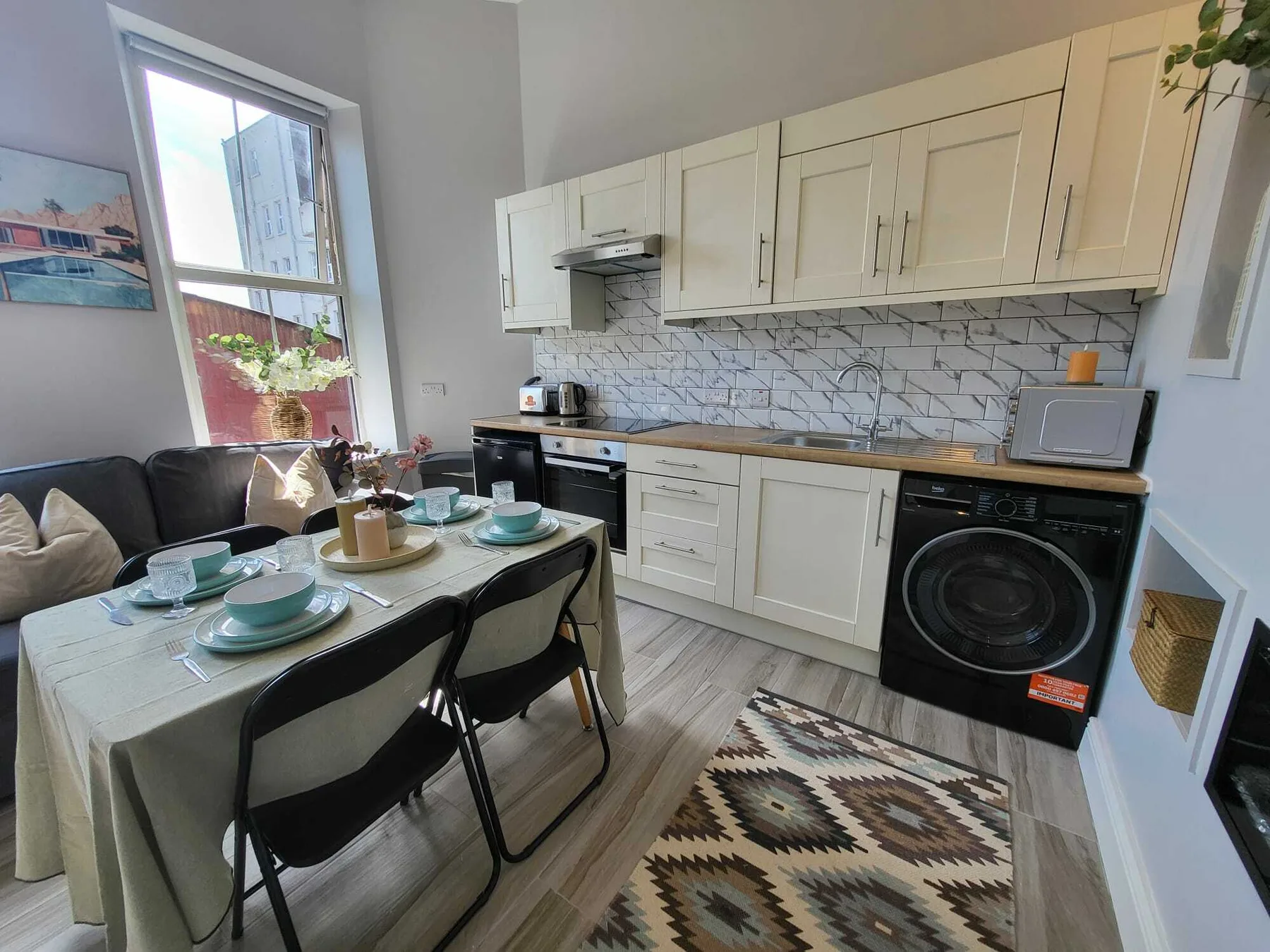 Una cocina y comedor compactos con una mesa puesta y armarios blancos.