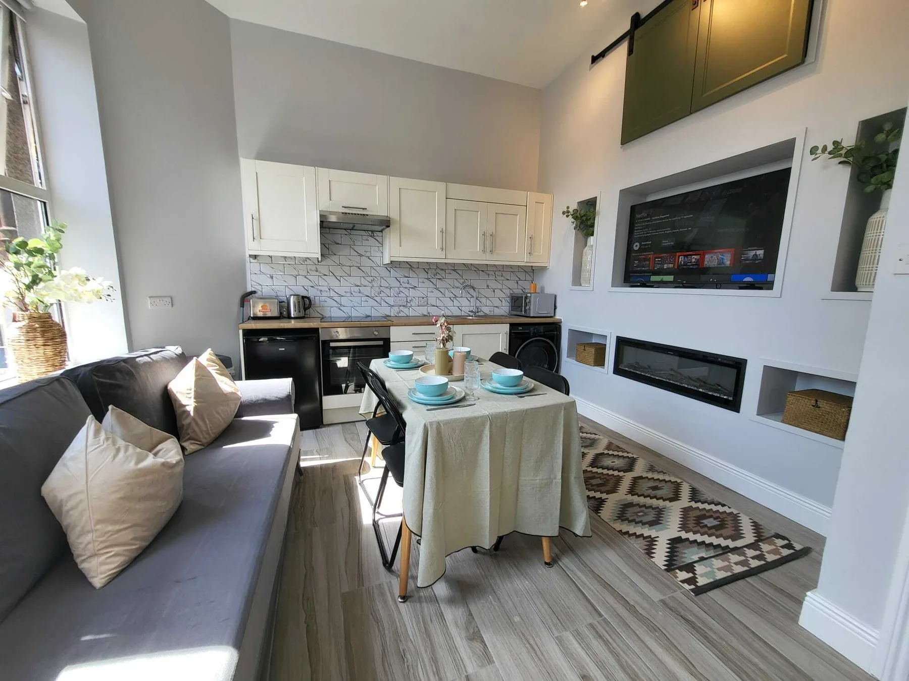 Una cocina y comedor luminosos con una mesa, asientos y electrodomésticos integrados.