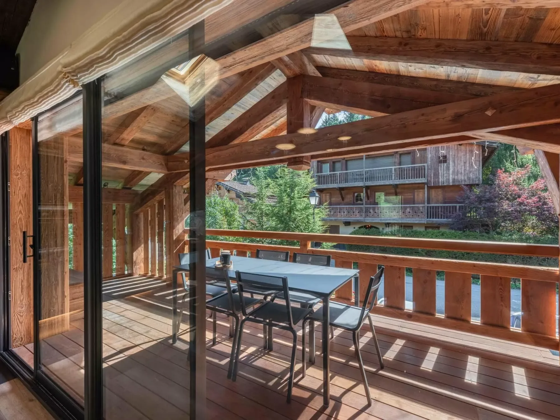 Una terraza cubierta de madera tiene una mesa de comedor y sillas con edificios y árboles al fondo.