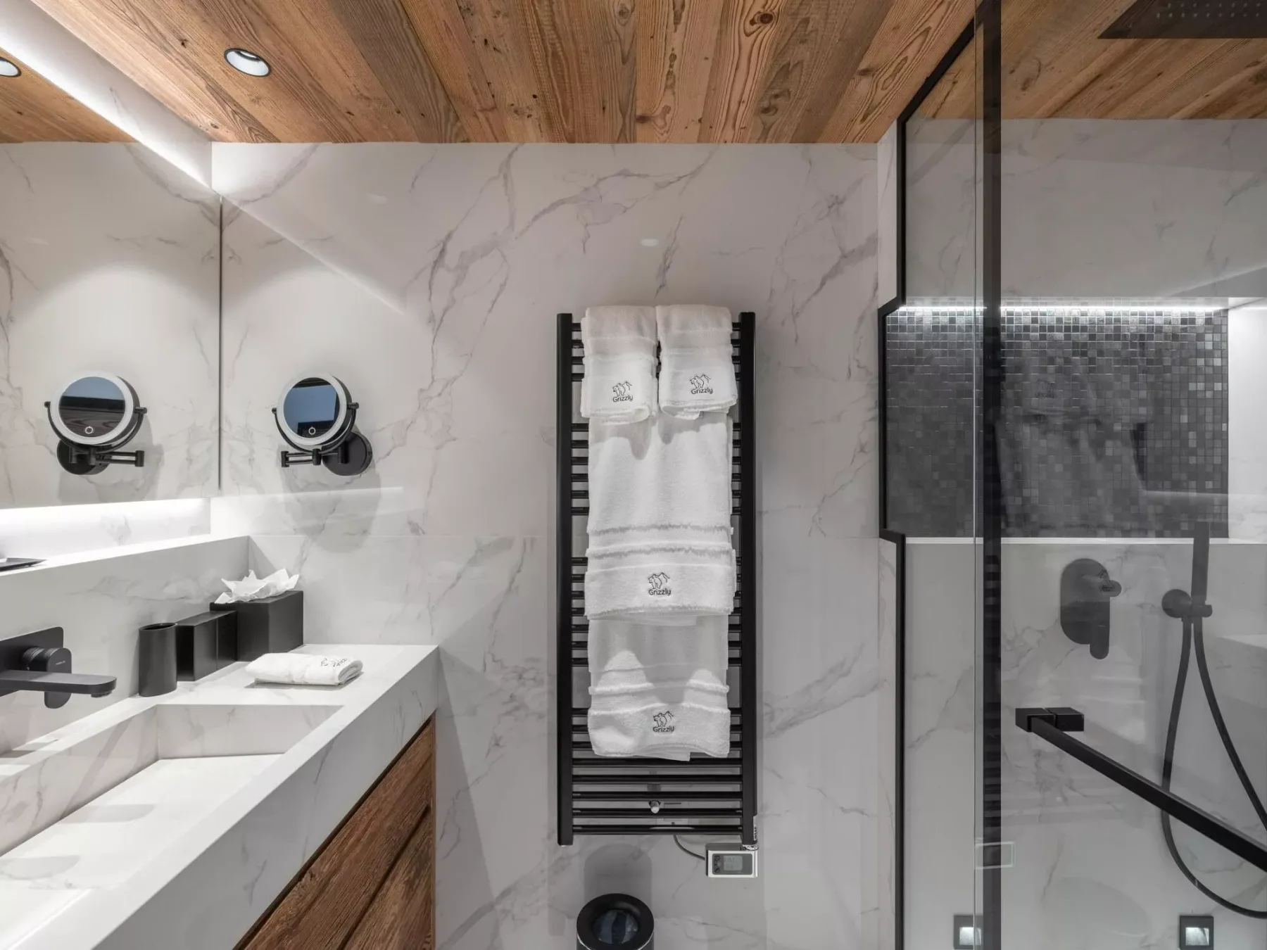 Baño revestido de mármol, con lavabo doble y ducha de vidrio.