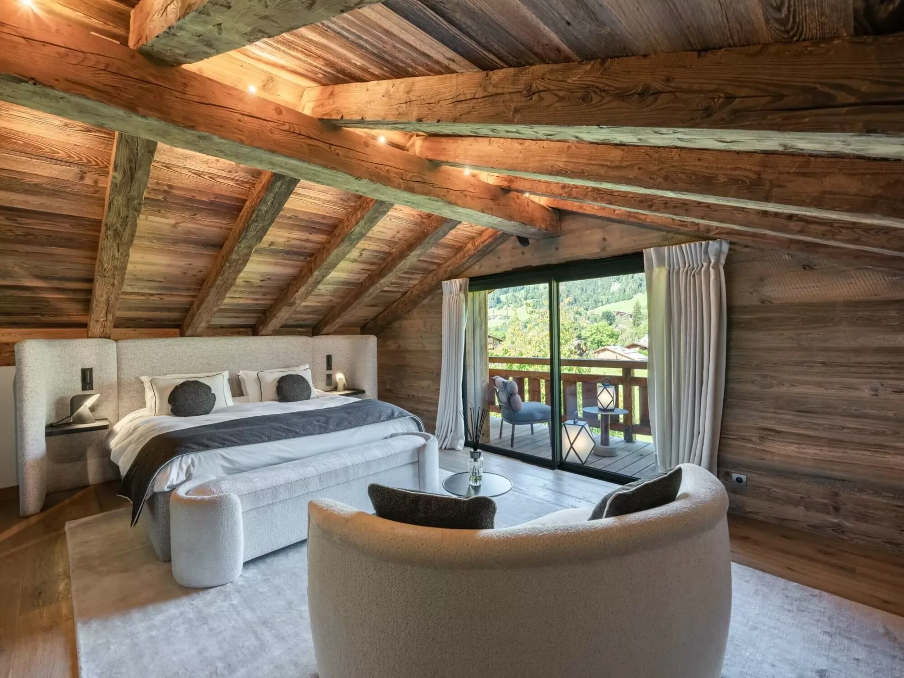 Dormitorio revestido de madera con cama, asientos curvos y puertas que dan a un balcón.