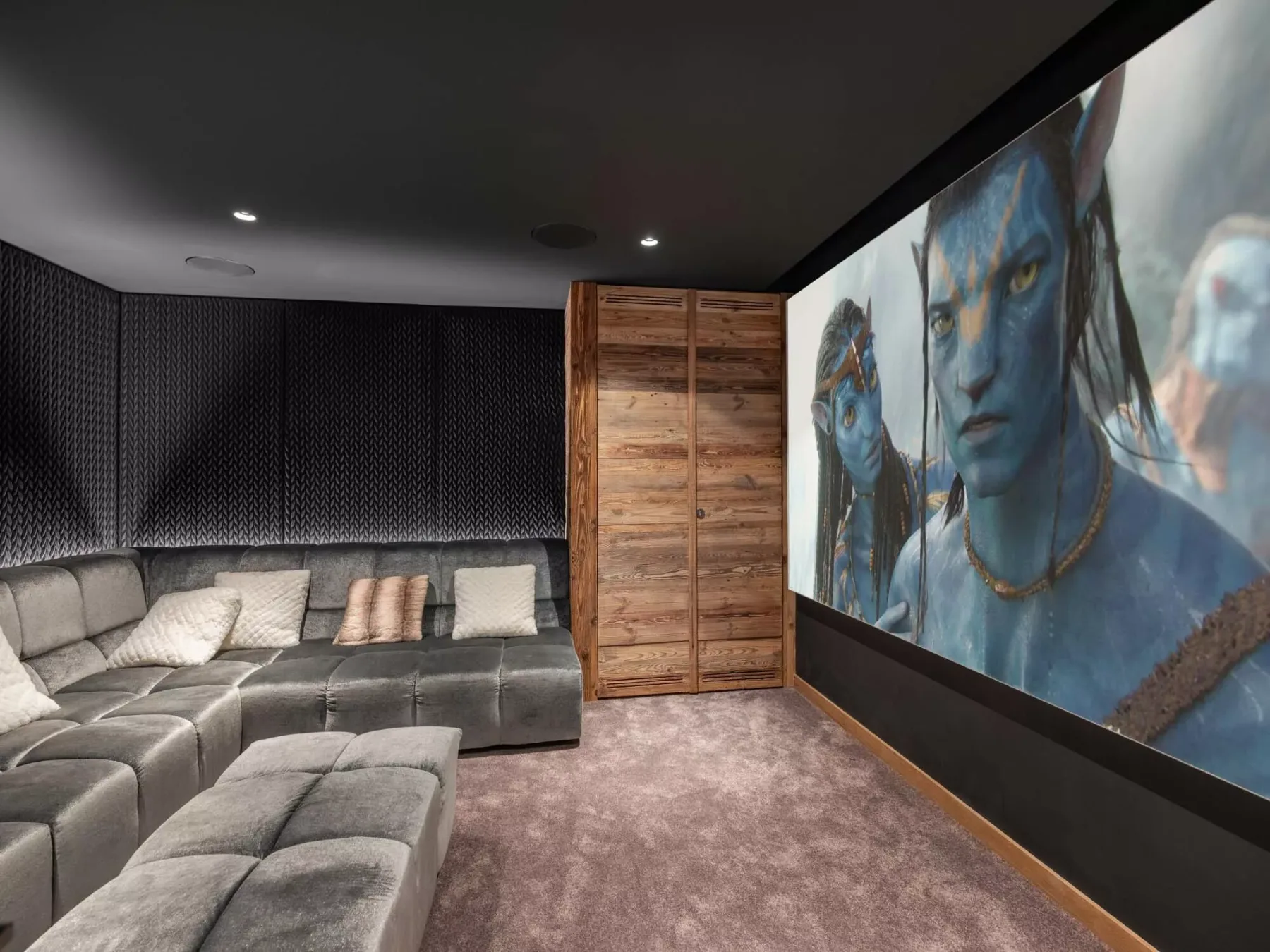 Una sala multimedia tiene un sofá seccional grande y una imagen de película en la pared.