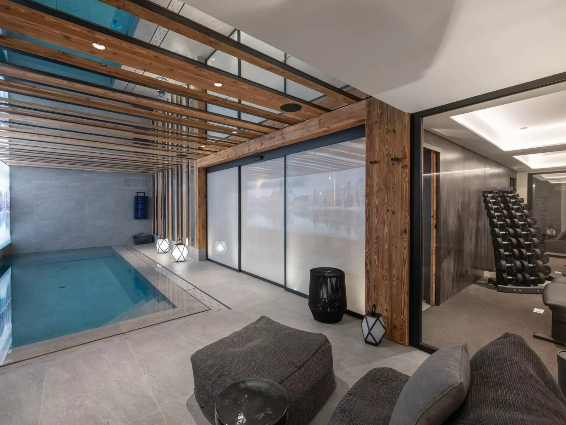 Una piscina interior junto a una zona de estar con asientos bajos y paredes de vidrio.