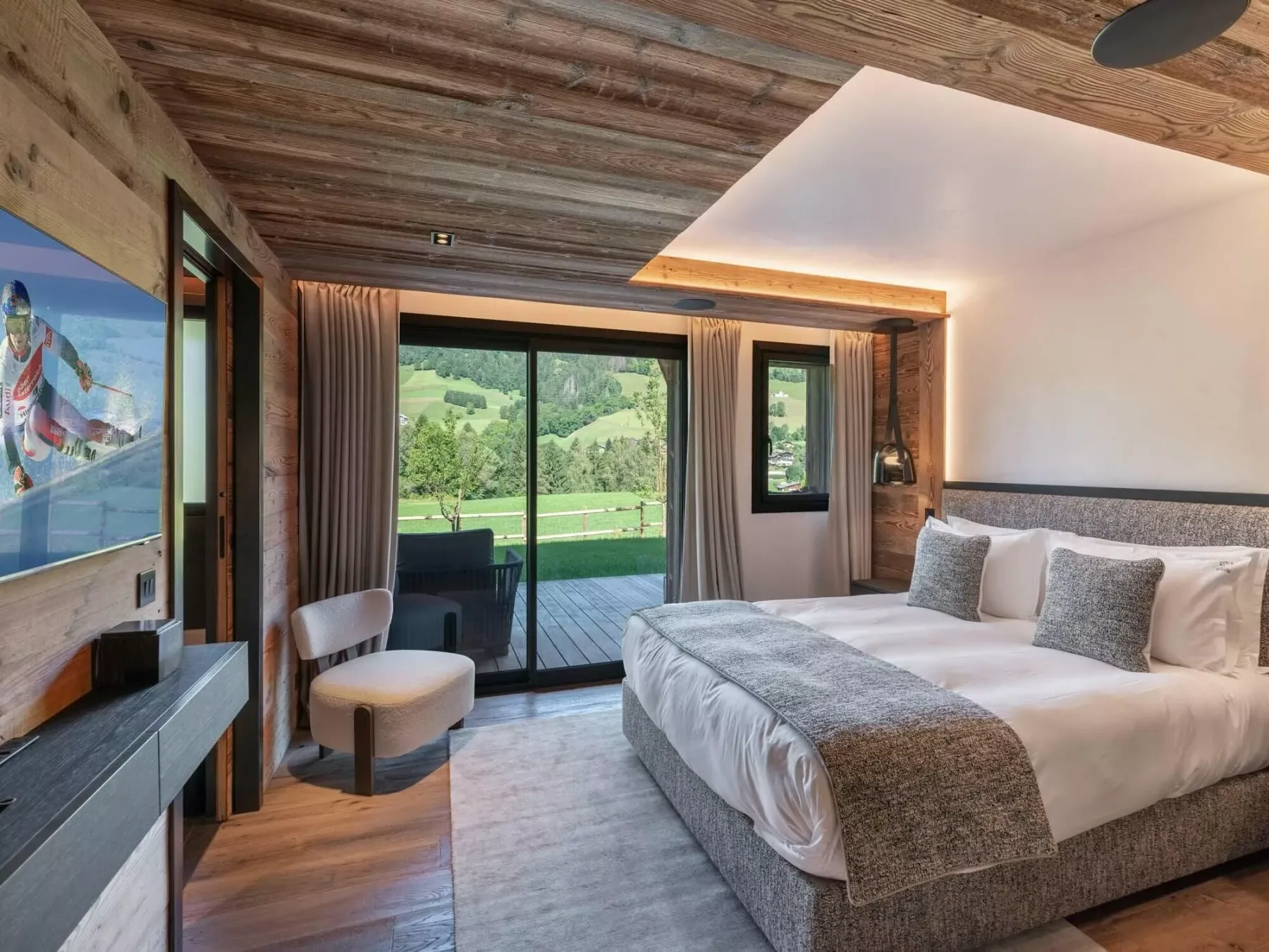 Un dormitorio con una cama grande junto a puertas de vidrio que dan a un paisaje verde.