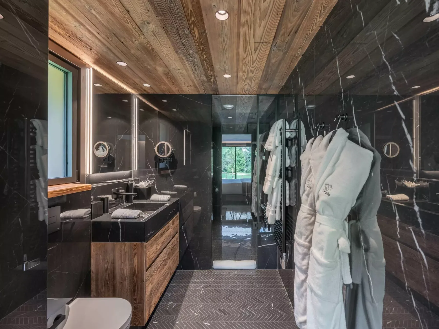 Un baño moderno con paredes oscuras, un mueble de madera y batas colgadas.