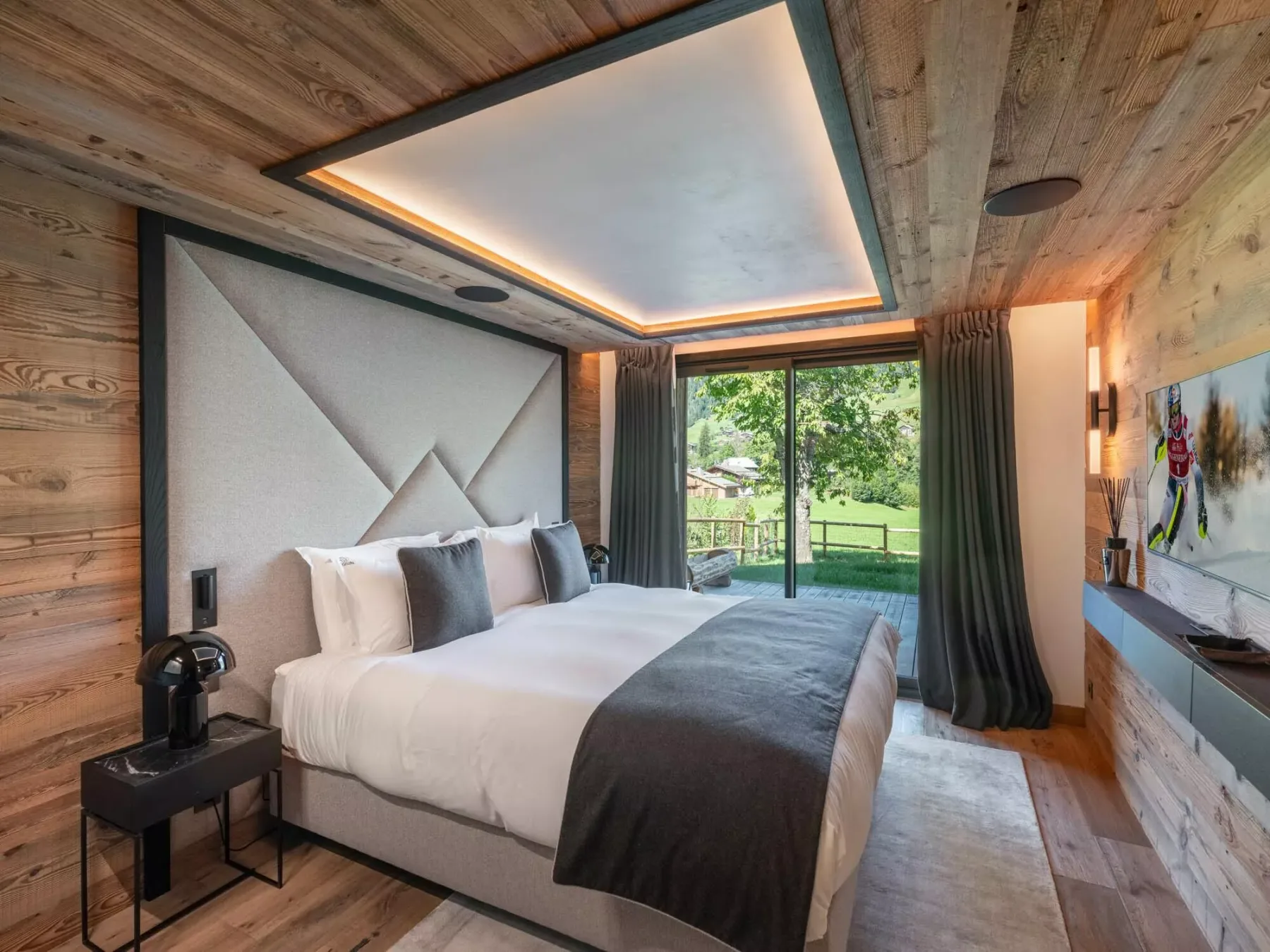 Un dormitorio con una cama grande frente a puertas de vidrio que dan a un área verde.
