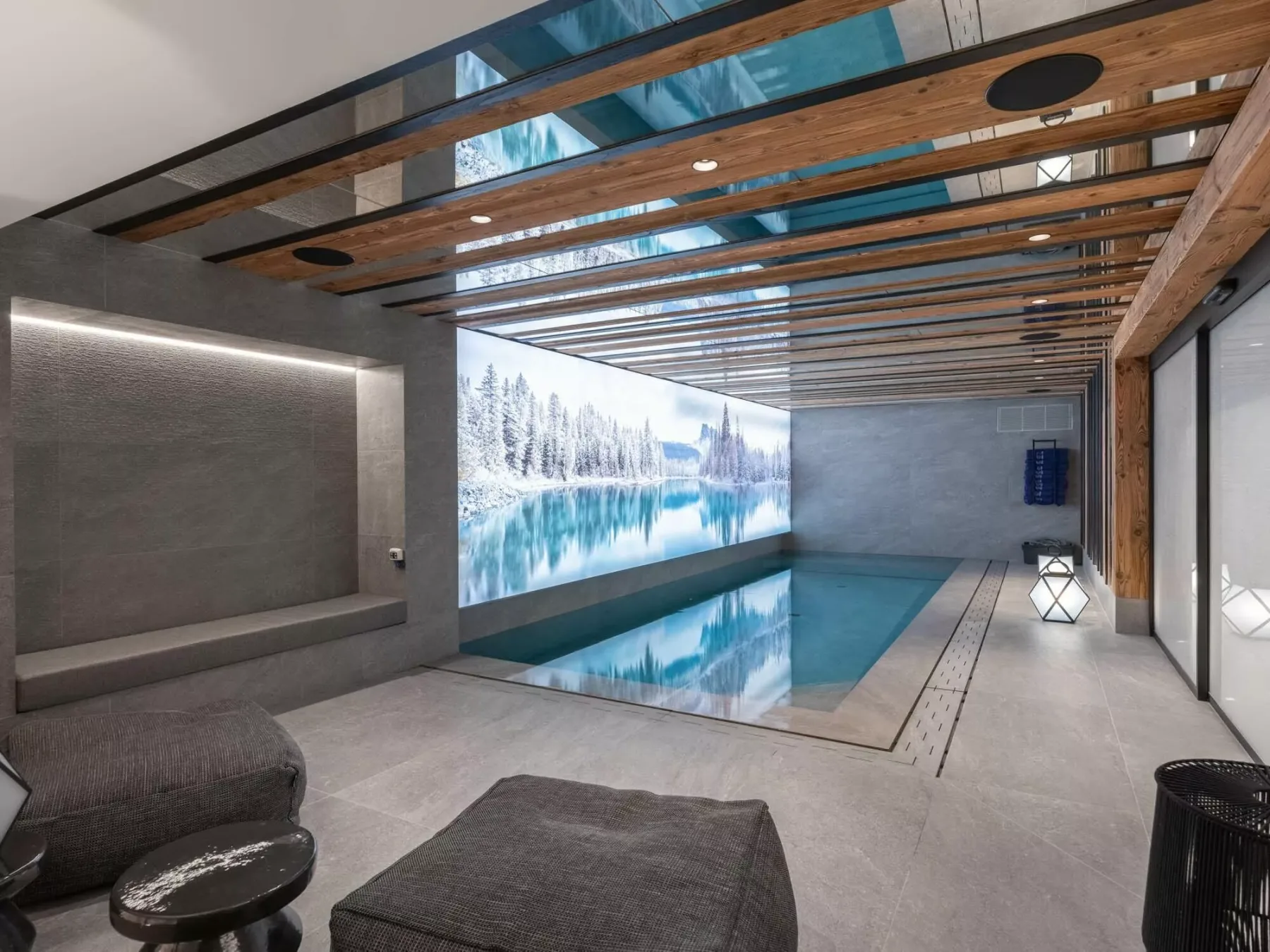 Una piscina interior está junto a asientos oscuros, bajo un techo con vigas expuestas.