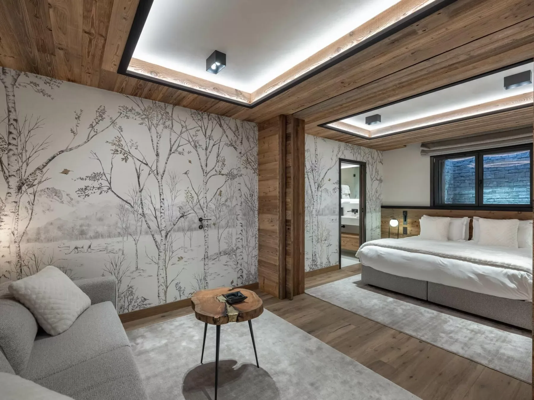 Un dormitorio con una cama y asientos grises junto a un mural.