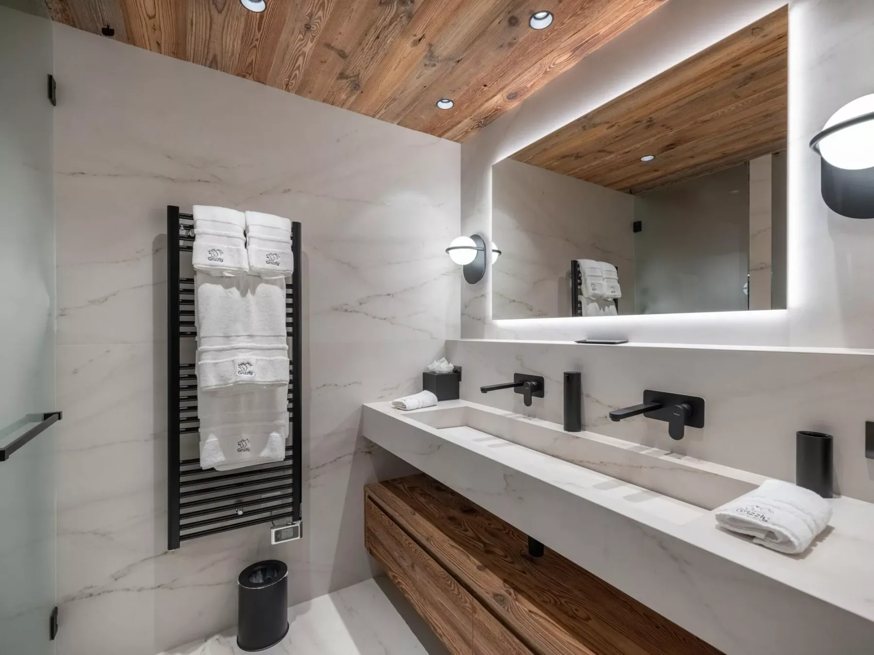 Un baño moderno con un tocador largo, un espejo de pared y techo revestido de madera.