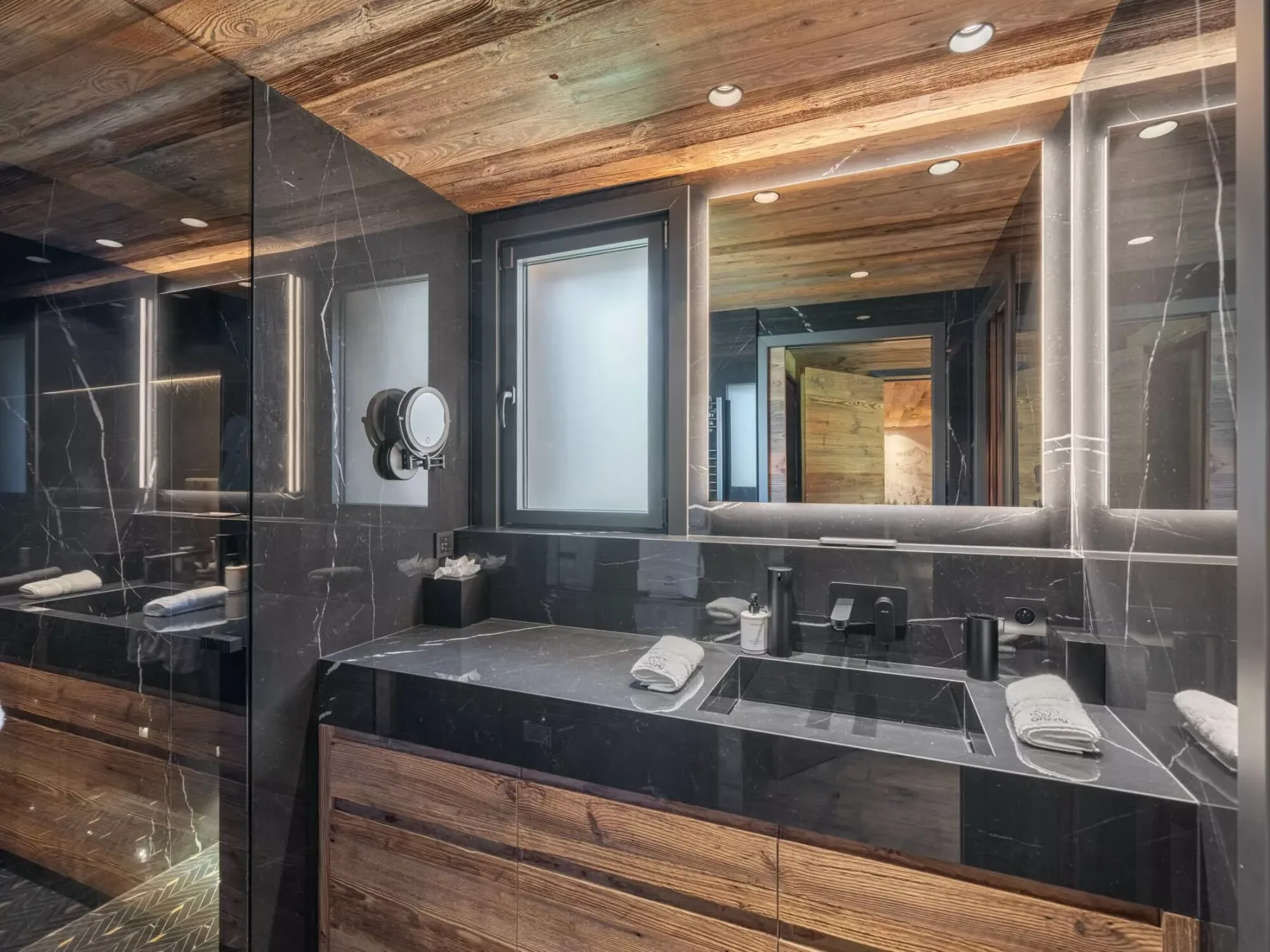 Un tocador de baño moderno con un espejo amplio y encimeras de piedra oscura.