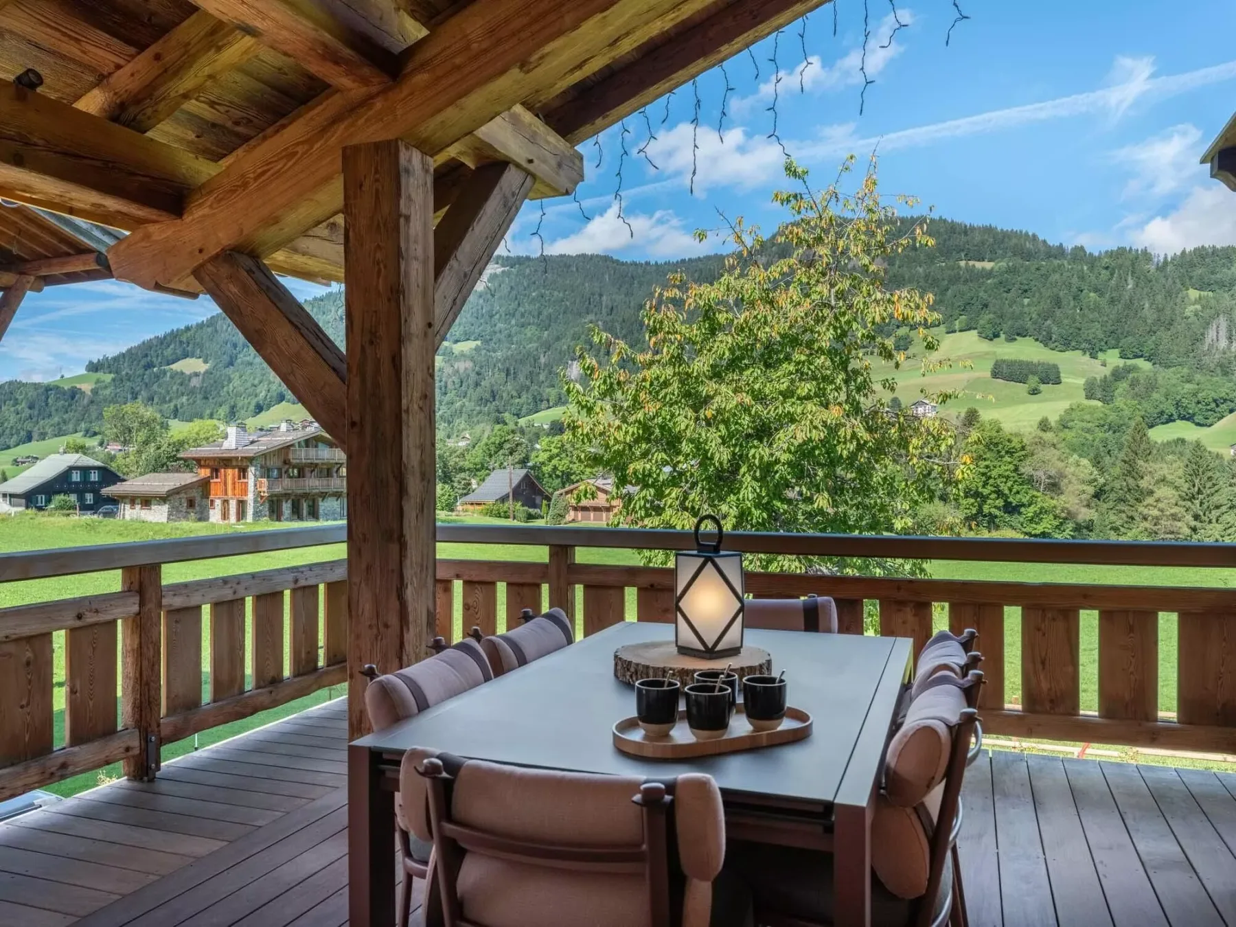 Una zona cubierta de comedor al aire libre, con mesa y asientos, da a un paisaje montañoso verde.